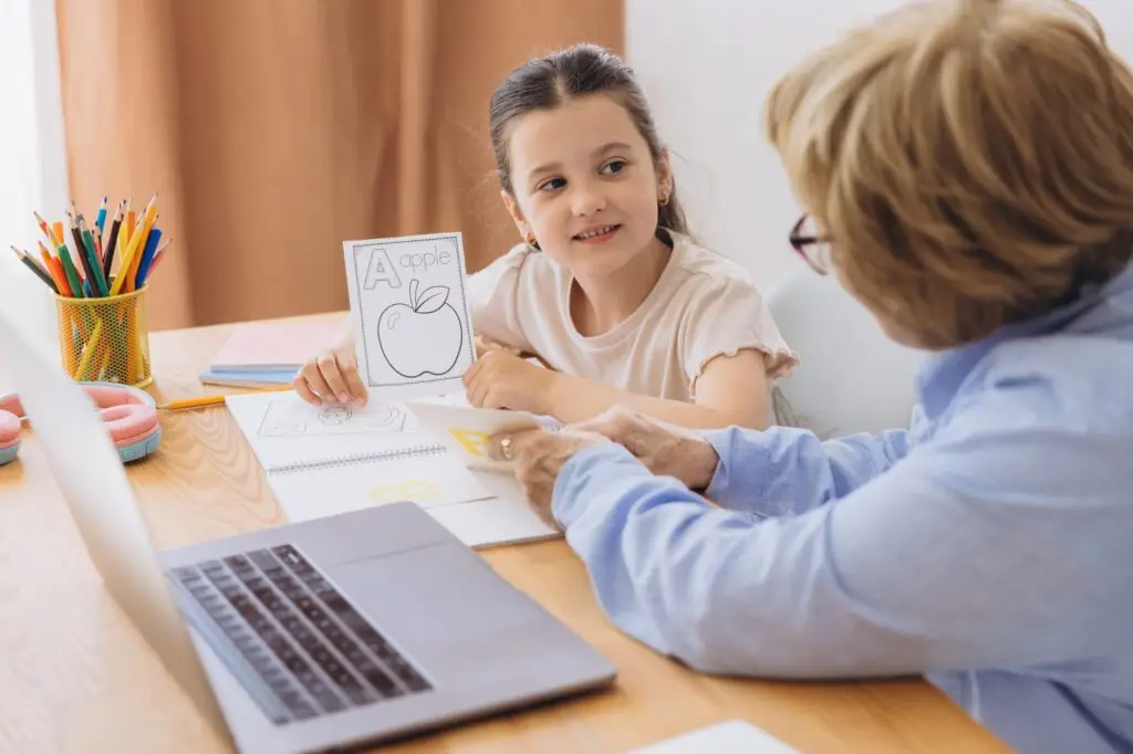 Happy grandma helping adorable preschool granddaughter school kid with homework task.